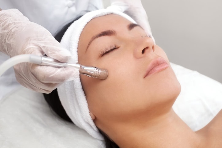 Woman at a spa receiving a microdermabrasion treatment from her therapist, who is a spa therapy graduate