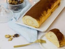 Eine frisch gebackene Maronenroulade ist am Kaffeetisch angerichtet. Ein Stück steht schon zum Essen bereit.