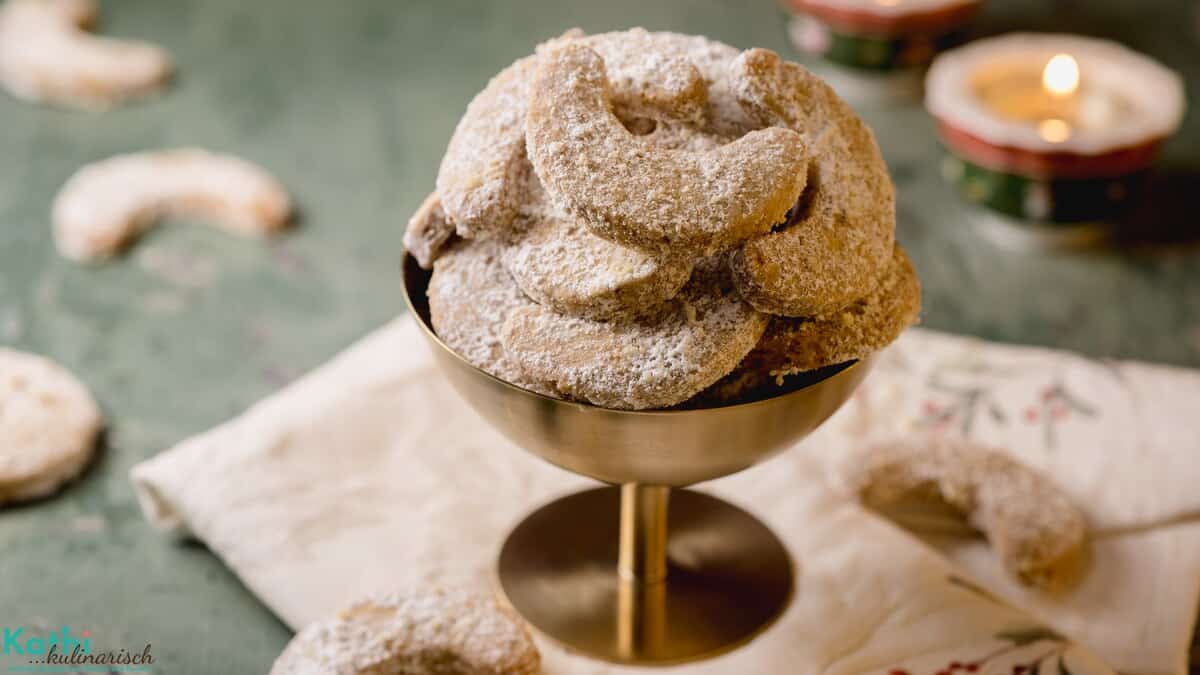Eine goldene Schale mit Stiel ist gefüllt mit Vanillekipferl nach einem Rezept von meiner Oma. Im Hintergund ist ein Teelicht zu sehen und ein paar Kipferl.