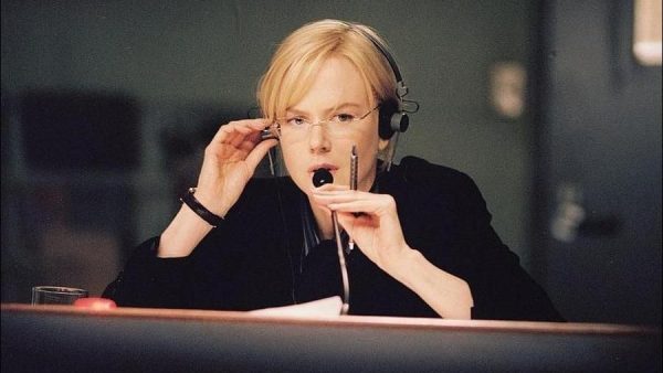 Nicole Kidman in a scene from 'The Interpreter'. She is wearing glasses, headphones and speaking into a microphone while holding a pen.