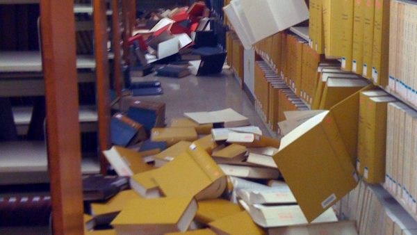 a library with books falling out of bookshelves and piled on the floor.