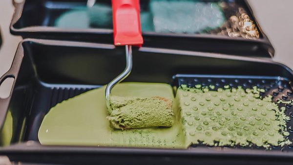 a roller sitting in a tray of green paint.