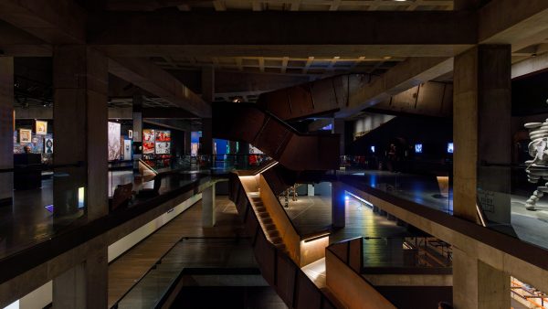 a cavernous darkly lit interior of a museum building with a large staircase in the middle of the picture.