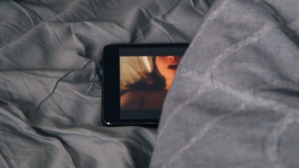 A black android phone on a grey bedspread that depicts a naked woman from the shoulders up.