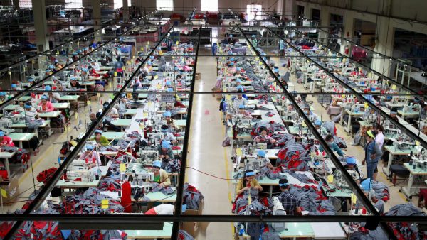 An overhead shot of a Cambodian garment factory, featuring several long lines of workers sewing tracksuit pants