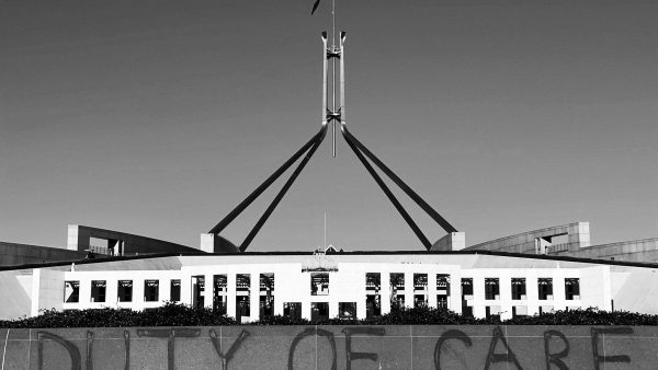 A black-and-white photograph of Parliament House in Canberra with the words "duty of care" spray-painted on a low wall in front.