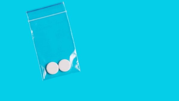 two round white pills in a clear plastic bag against a bright blue background