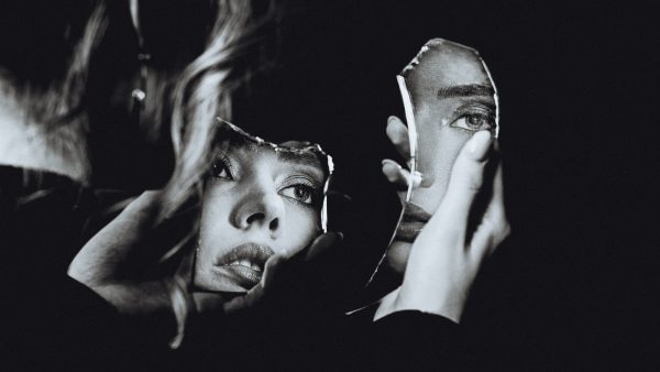 a black and white photograph of a woman holding two shards of a mirror. Her face is reflected in both pieces from different angles.
