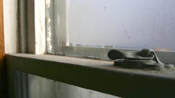 A dusty windowsill, with the latch in the foreground.