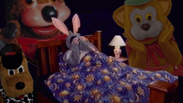 a composite image of Bakana Bilby (a person in a full-size Bilby suit) in a bed with hands over his eyes, with images of Big Dog, Fat Cat and Doopa Dog positioned around the bed like ghosts or sleep paralysis demons.