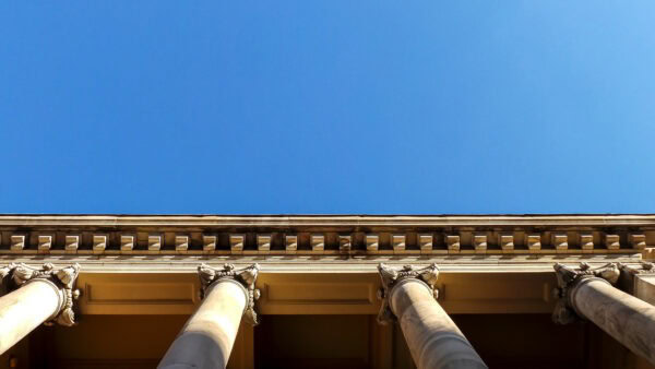 A photo taken looking upwards of the columns of the old Adelaide Supreme Court building against a blue sky.