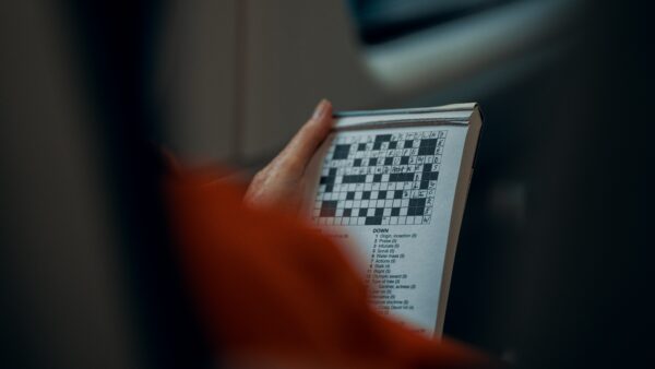 A shot from over a person's shoulder of them holding a tear-off pad with a half-completed crossword on it.