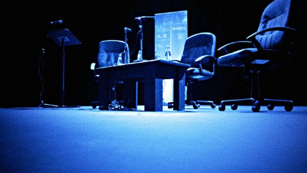A collection of empty chairs on stage at a writers festival, surrounded by a small table, microphones, a banner and a lectern.
