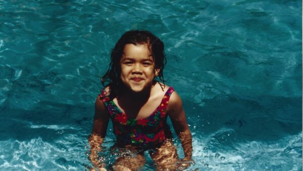 a photograph of a young dark-skinned girl in a red swimsuit smiling in a pool.