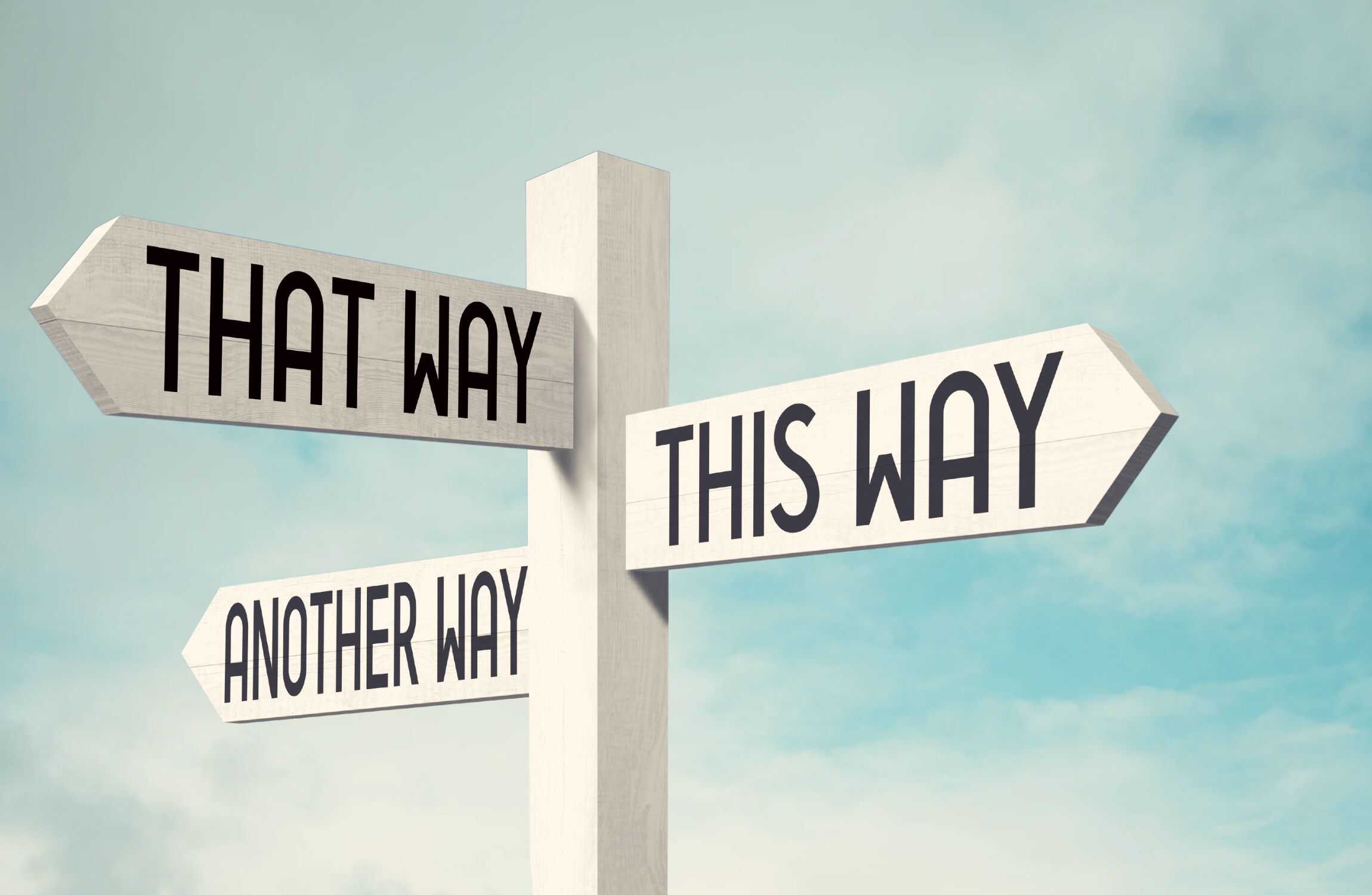 A white timber signpost against a blue sky, with arrows saying "THAT WAY", "THIS WAY" and "ANOTHER WAY" all pointing in different directions.