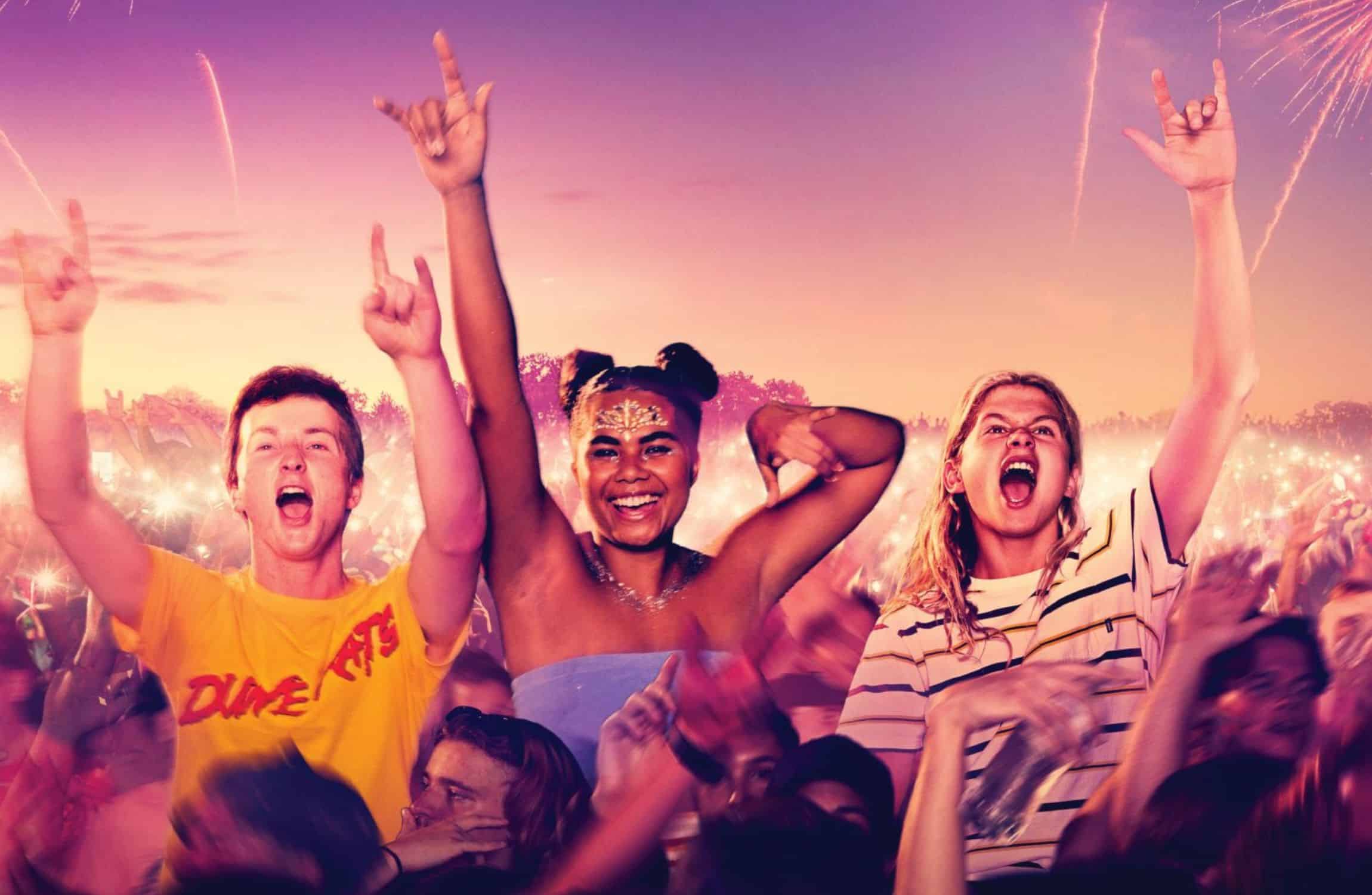 Three friends dance and make 'rock on' hand symbols in a music festival crowd.