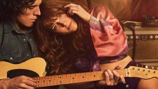 A man sits, playing an electric guitar, as a woman with long hair leans on his shoulder.