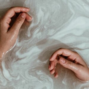 Two hands rest in soapy bathwater.