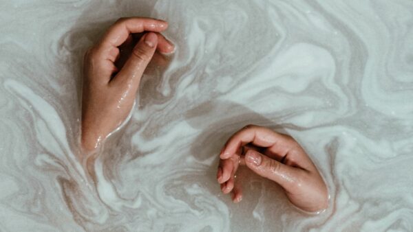 Two hands rest in soapy bathwater.