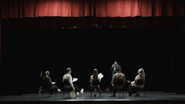 A theatre group do a read through on a stage.