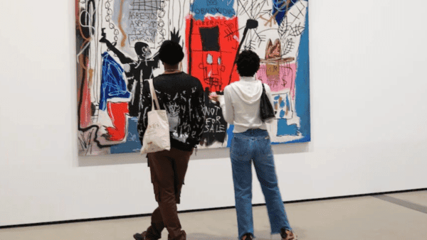 Two young Black people look at a large painting by Jean-Michel Basquiat hanging in a gallery. In the bottom, in the middle, it reads: Not for Sale.