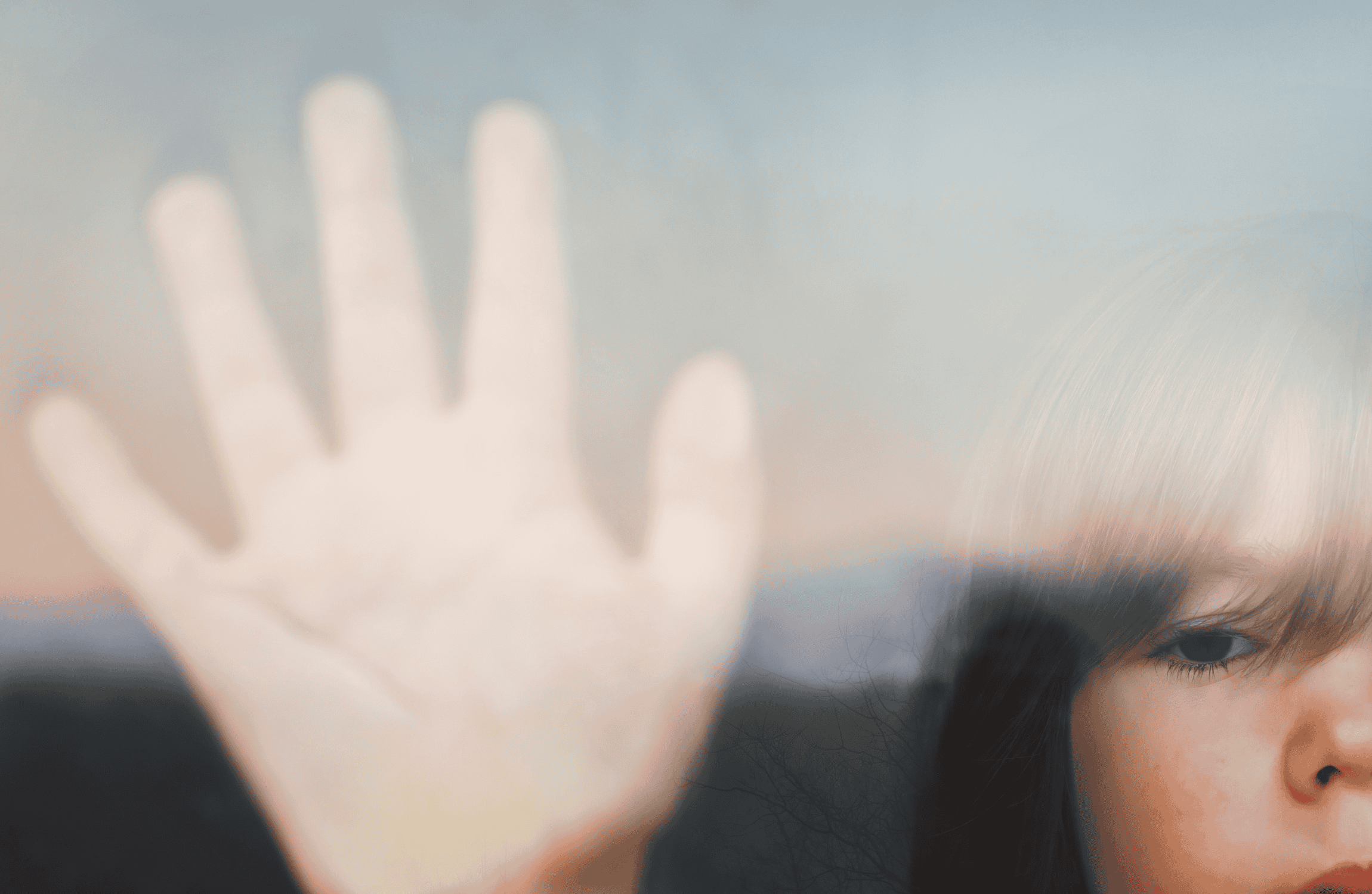 A child stands at a window with their palm against the glass.