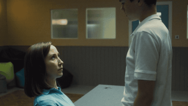 A still from the TV show 'Adolescence'. A boy in a white shirt stands over a woman in a blue shirt.