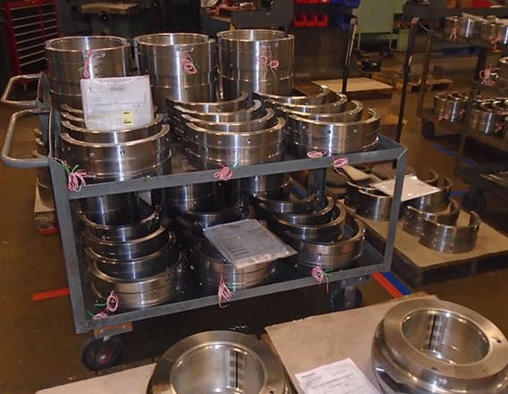 Two carts filled with naval bearings showing they have been wired. Surrounding the carts are pallets of naval bearings that are not wired.