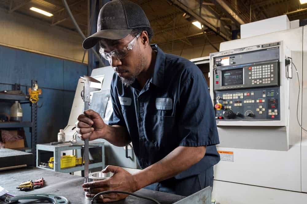 Team member Pierre measures a small bearing (about 5" OD) with a gauge at work station.