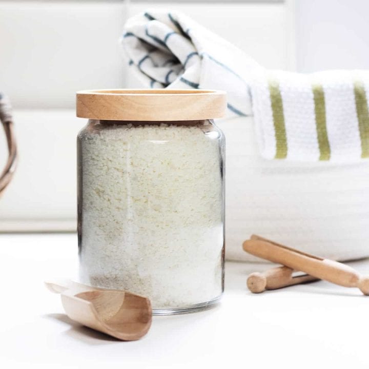 Large jar filled with homemade laundry detergent with a wooden scoop and clothespins next to it.