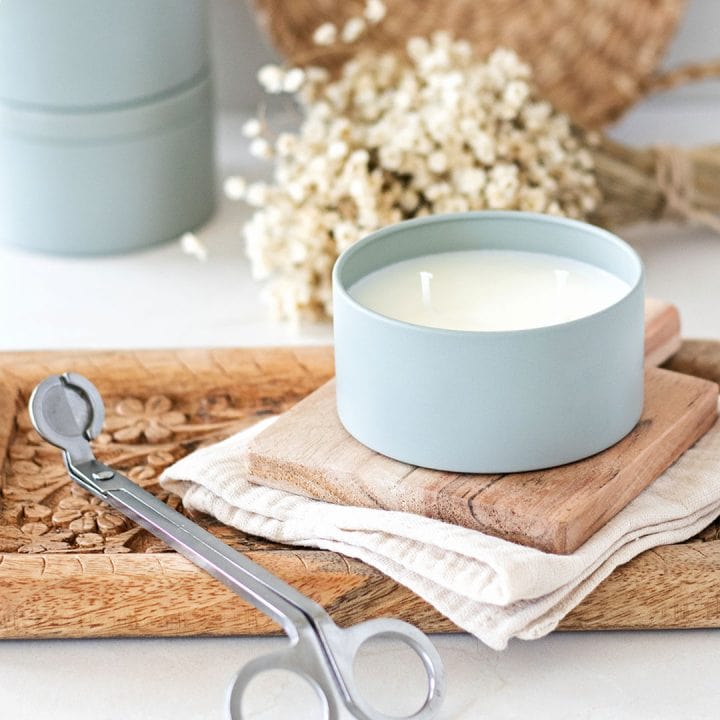 Double wick candle in a sage blue candle tin ontop of wood boards next to a candle wick trimmer.