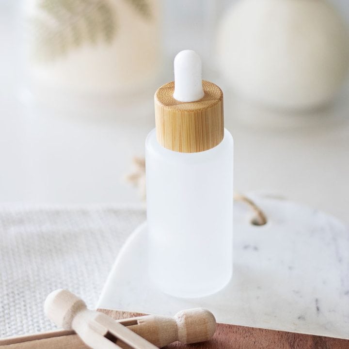 frosted glass bottle with a bamboo dropper of a laundry scent booster in front wool dryer balls behind wooden clothes pin