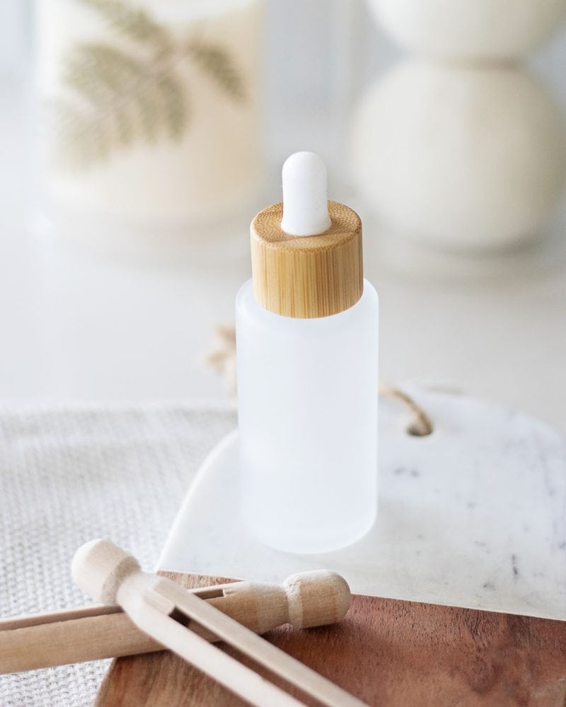 frosted glass bottle with a bamboo dropper of a laundry scent booster in front wool dryer balls behind wooden clothes pin