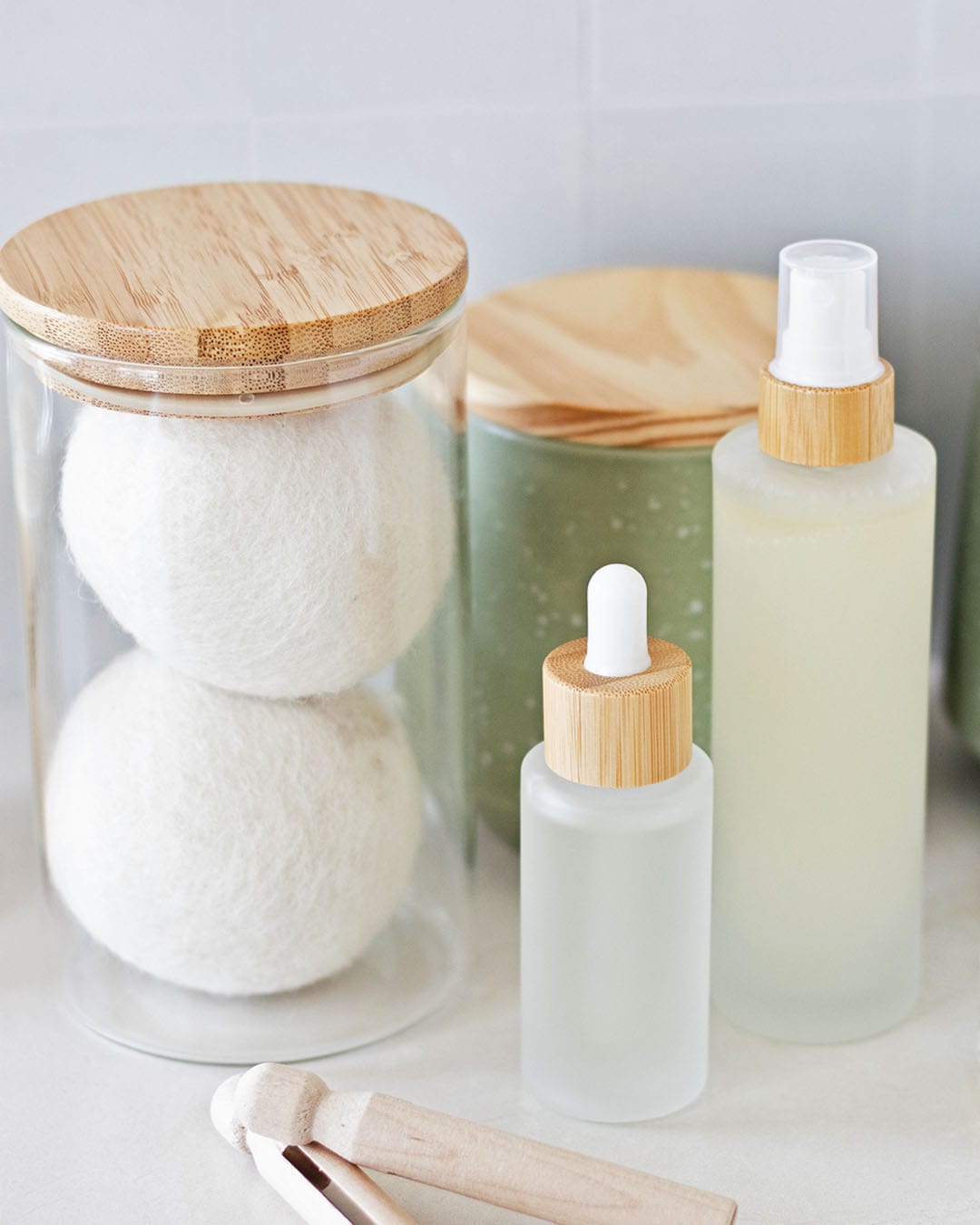 laundry room counter with a glass jar of wool dryer balls, wooden clothespins, and homemade bottles of linen spray and laundry scent booster.