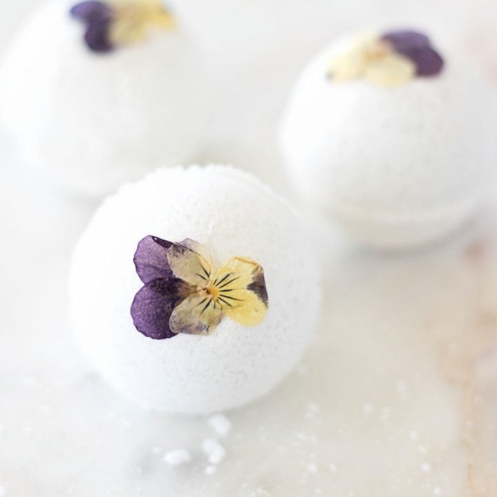 three pressed violet pansy flowers on bath bombs on a marble counter