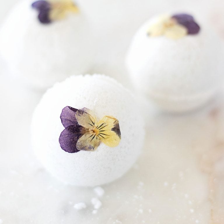 three pressed violet pansy flowers on bath bombs on a marble counter
