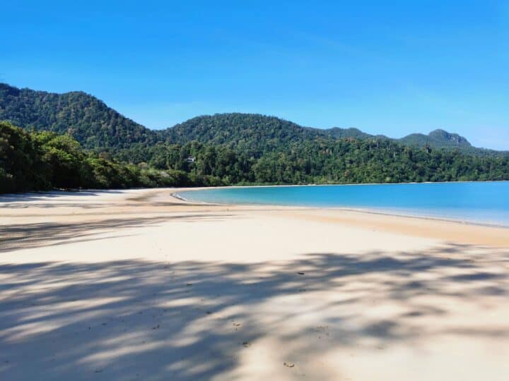 Panoramic tropical beach scene on Langkawi Island with turquoise sea, white sand and lush green hills under a bright blue sky