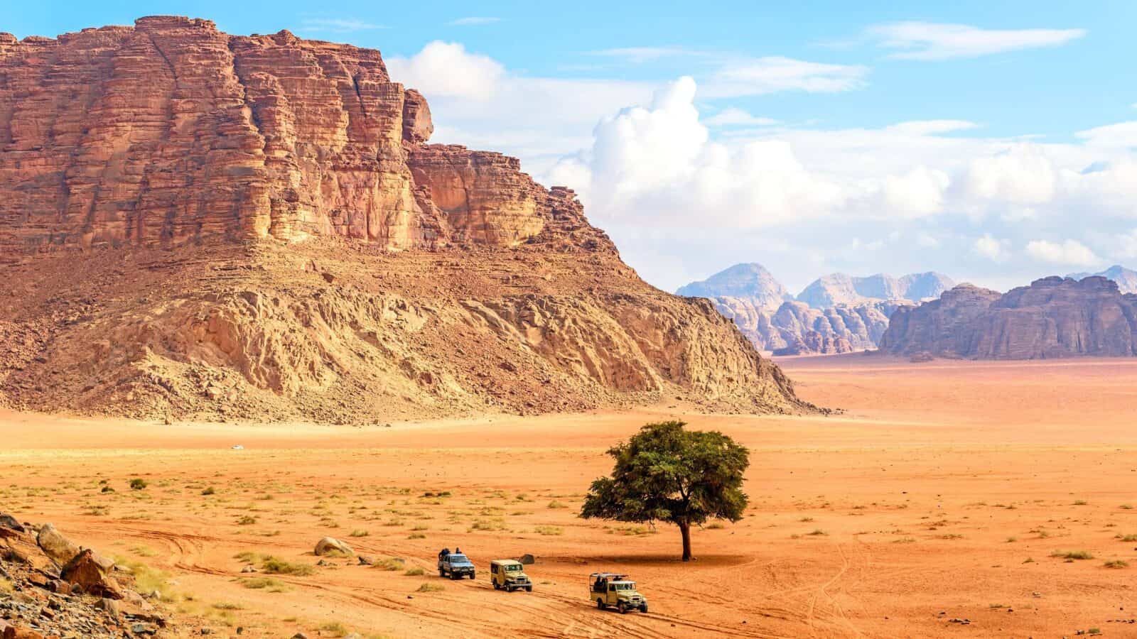 4x4 jeep driving across red sand dunes among towering rock formations in Wadi Rum desert