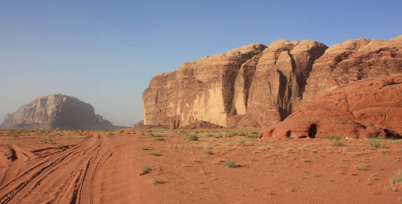 Off-road jeep and camels crossing the red sand dunes and rock formations of Wadi Rum desert