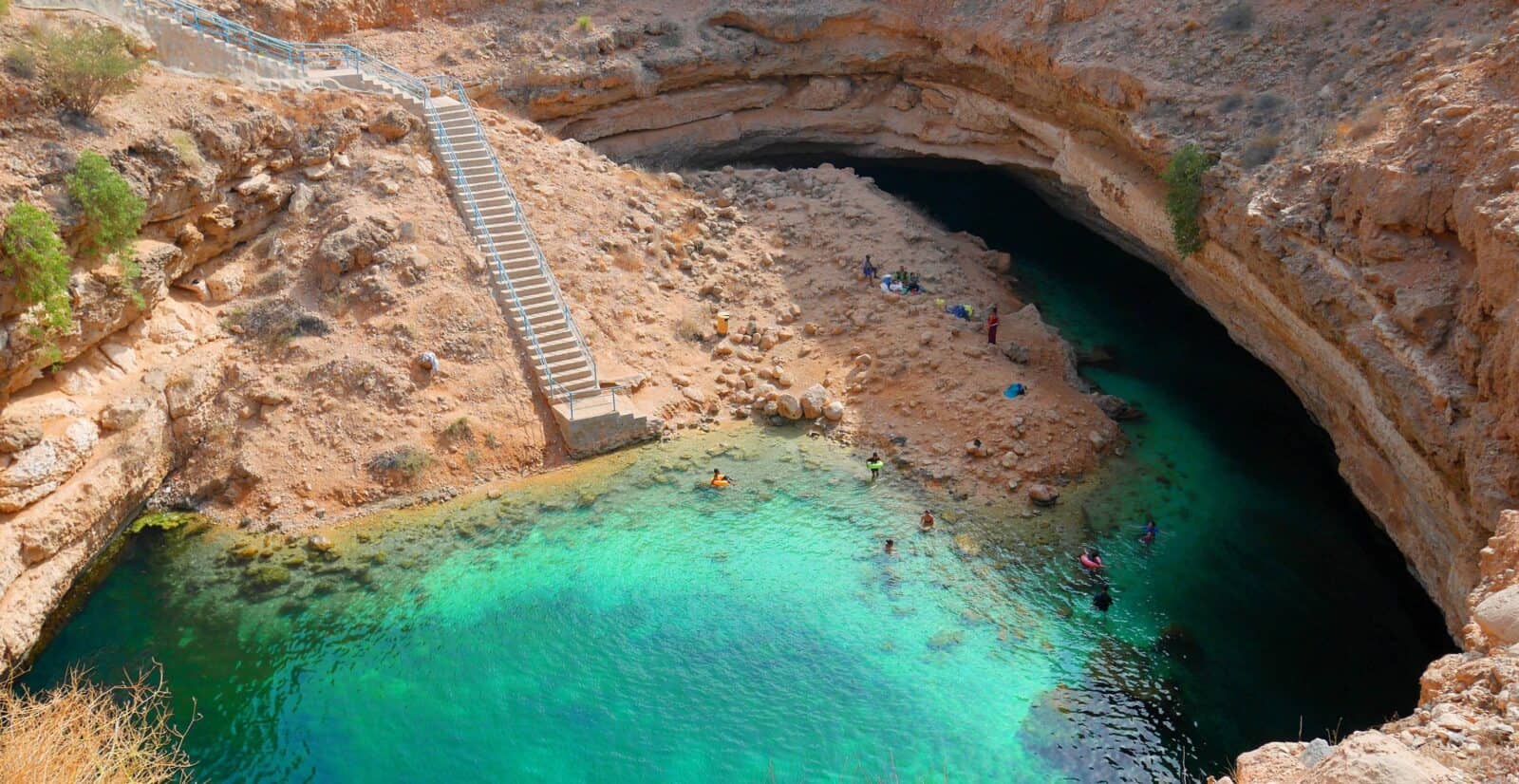 Aerial view of Bimmah Sinkhole in Oman with turquoise water surrounded by limestone walls and palm trees