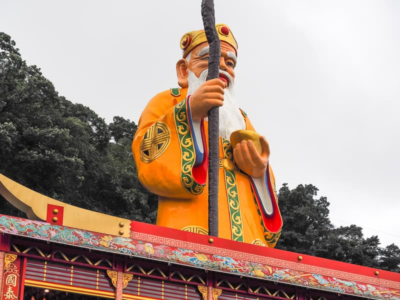 A statue of a bearded old man Tudi Gong, the Earth God, holding a staff on the side of a mountain