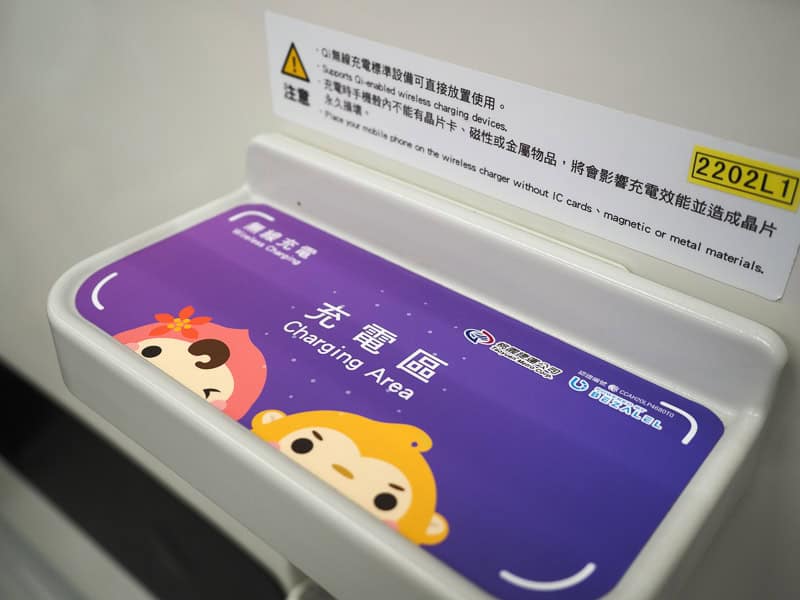A flat panel on the side of an Airport MRT meant for charging a phone, with purple sticker, words, and two cute little characters on it