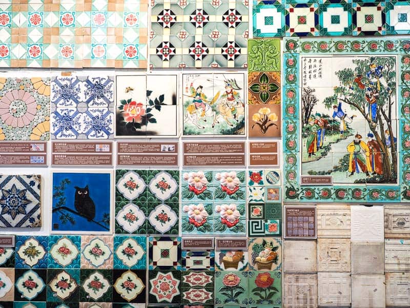 A wall covered in various artistic tiles with different patterns include one of a traditional Chinese scene