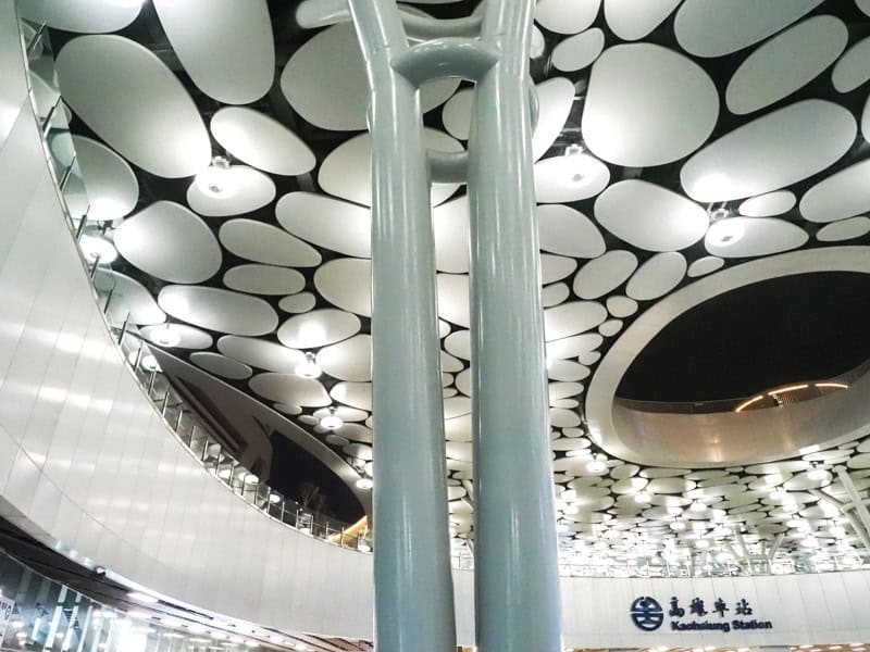 Inside Kaohsiung train station, with tall pylons up to a beautifully patterned ceiling