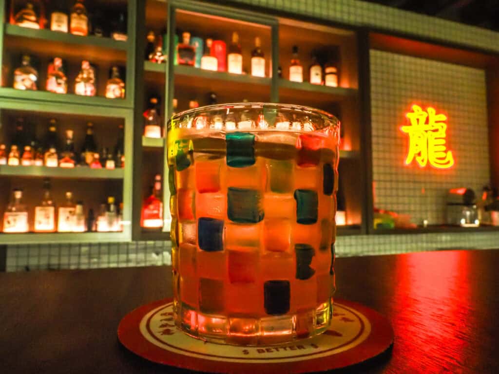A cocktail in a colorful glass inside a small cocktail bar in Tainan with neon Mandarin character on the wall beside the bar
