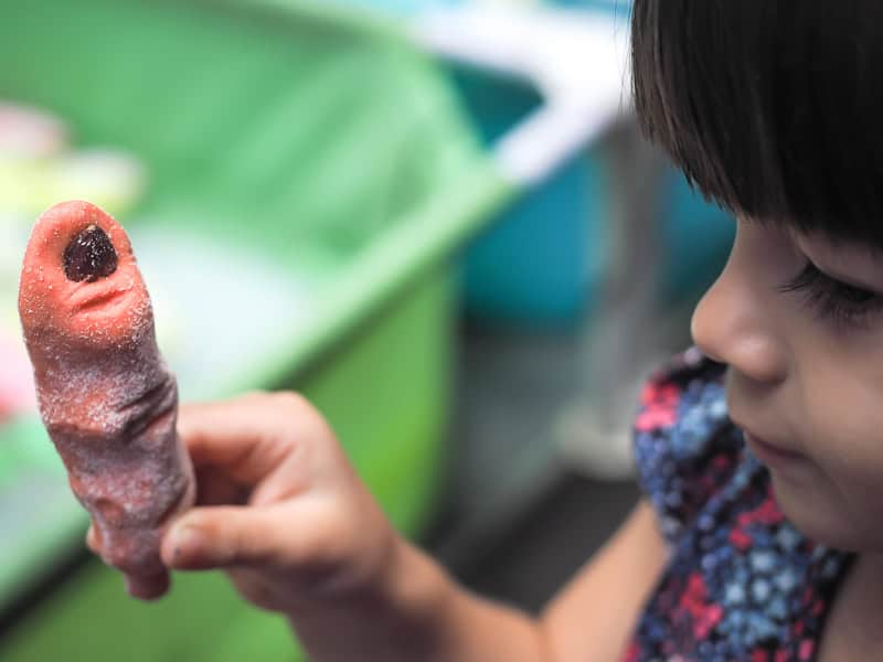 A girl holding up a pink cookie shaped like a wtch finger