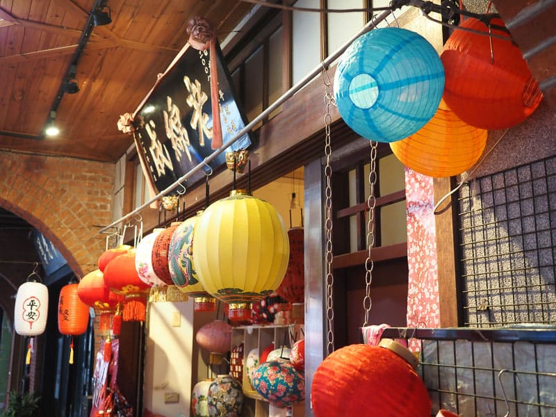 A traditional Chinese looking storefront with several colorful lanterns hanging around the entrance