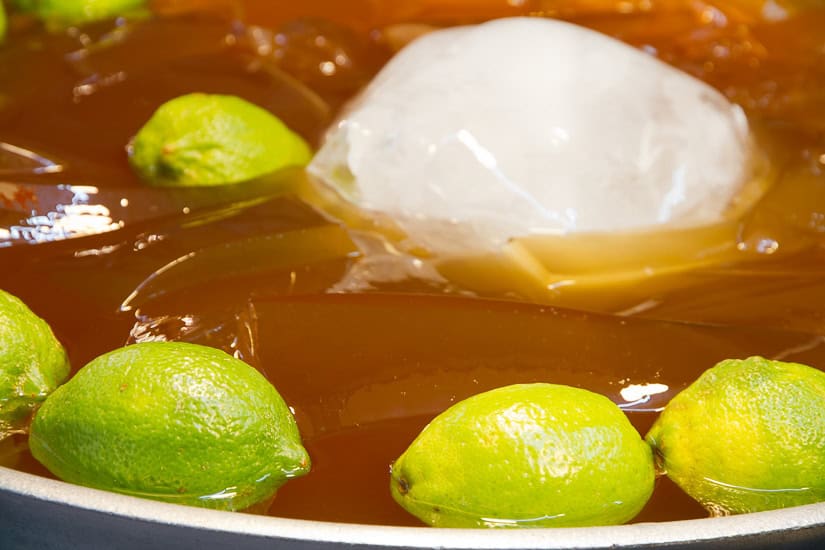 Close up of a bowl of brown colored jelly with floating ice chunk and whole green lemons