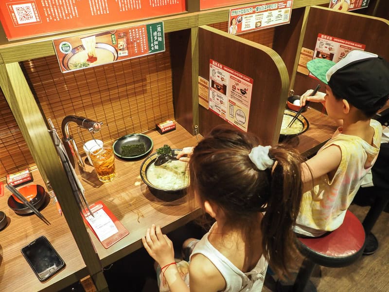 Two kids eating ramen at individual booths