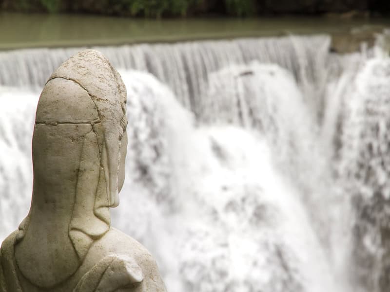 The back of a statue's head with a very wide waterfall as the background